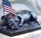 A statue of a dog lying down with a flag

Description automatically generated